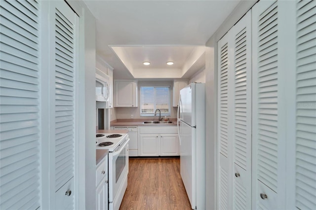 kitchen with wood-type flooring, sink, white cabinets, a raised ceiling, and white appliances