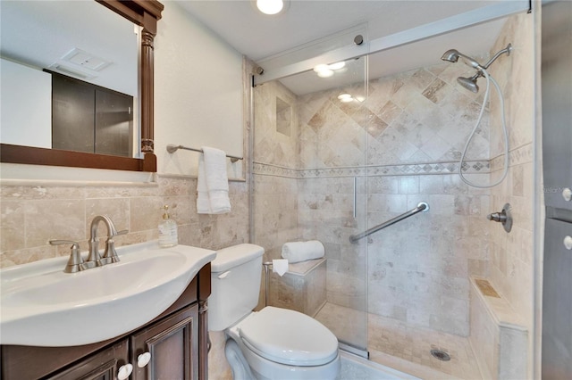 bathroom featuring vanity, toilet, a shower with shower door, and tile walls