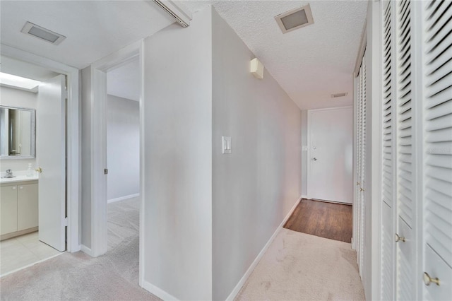 hallway with light colored carpet and a textured ceiling