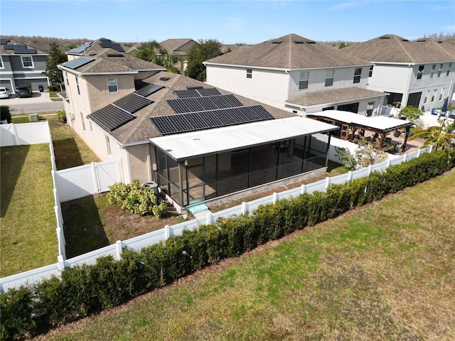 back of house featuring a lawn, a sunroom, and solar panels