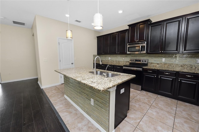 kitchen featuring appliances with stainless steel finishes, tasteful backsplash, sink, hanging light fixtures, and a center island with sink