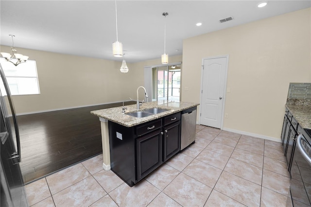 kitchen with pendant lighting, sink, appliances with stainless steel finishes, a kitchen island with sink, and light stone counters