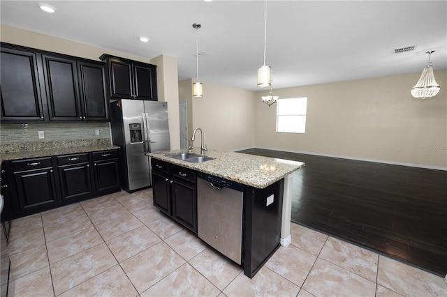 kitchen with sink, hanging light fixtures, stainless steel appliances, light stone countertops, and a kitchen island with sink