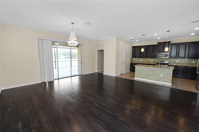 kitchen with tasteful backsplash, appliances with stainless steel finishes, hanging light fixtures, and a center island with sink