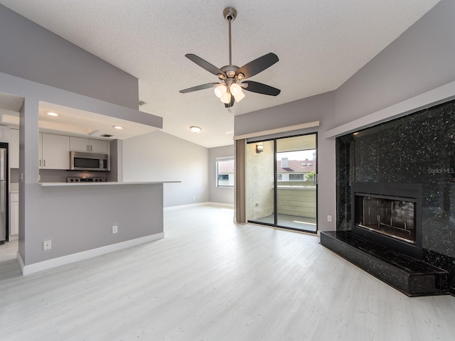 unfurnished living room with lofted ceiling, a textured ceiling, ceiling fan, a high end fireplace, and light hardwood / wood-style floors