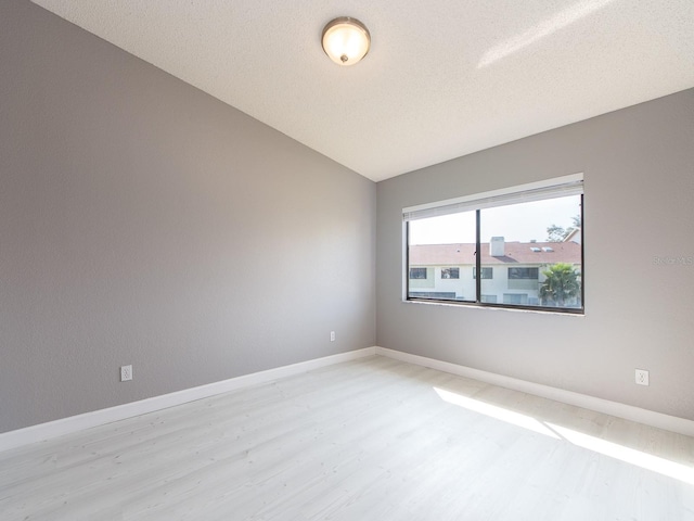 unfurnished room featuring lofted ceiling, light hardwood / wood-style flooring, and a textured ceiling