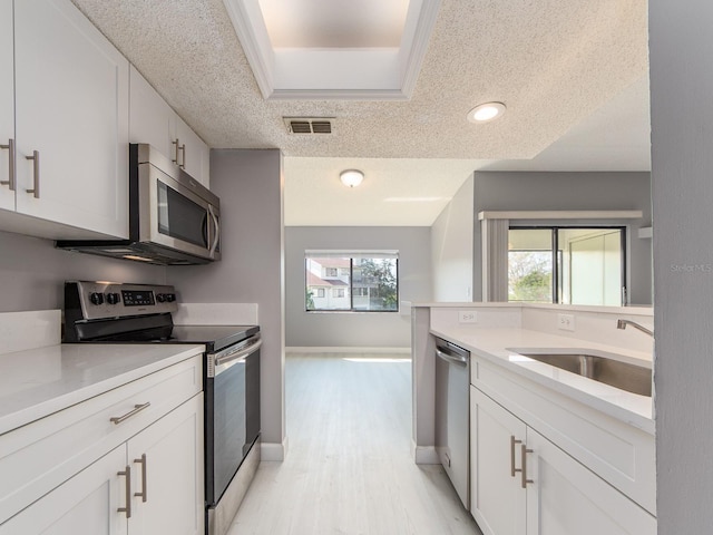 kitchen with white cabinetry, sink, stainless steel appliances, a textured ceiling, and light hardwood / wood-style flooring