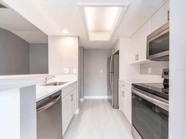 kitchen featuring sink, appliances with stainless steel finishes, a textured ceiling, white cabinets, and light wood-type flooring