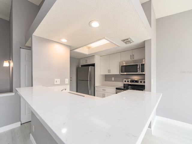 kitchen featuring sink, light wood-type flooring, kitchen peninsula, stainless steel appliances, and a textured ceiling