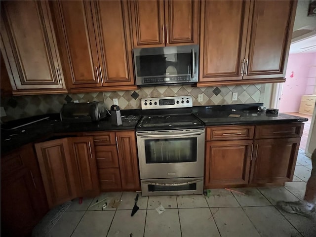 kitchen featuring dark stone countertops, light tile patterned floors, decorative backsplash, and appliances with stainless steel finishes