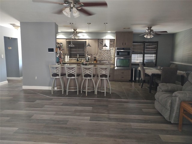 kitchen with a kitchen bar, decorative light fixtures, kitchen peninsula, stainless steel double oven, and backsplash