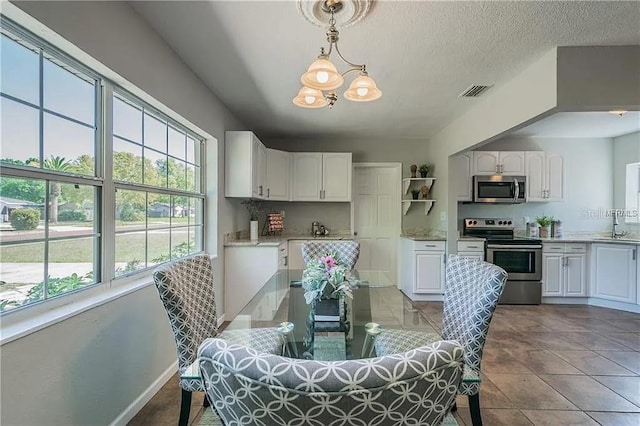 dining area with a notable chandelier, light tile patterned floors, sink, and a textured ceiling