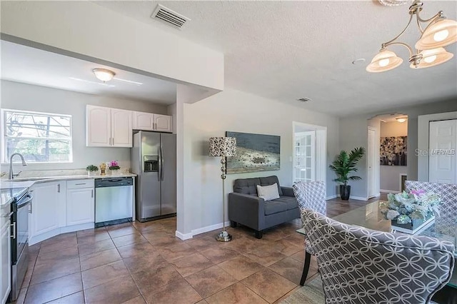 kitchen featuring sink, white cabinetry, hanging light fixtures, a textured ceiling, and stainless steel appliances