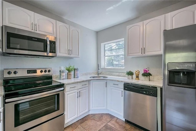 kitchen featuring sink, light tile patterned floors, stainless steel appliances, light stone countertops, and white cabinets