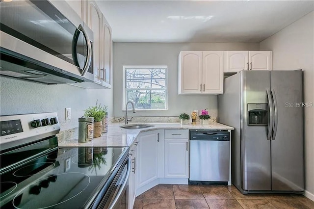 kitchen with white cabinetry, sink, dark tile patterned flooring, light stone counters, and stainless steel appliances