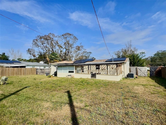 rear view of house featuring central AC unit, a lawn, and solar panels