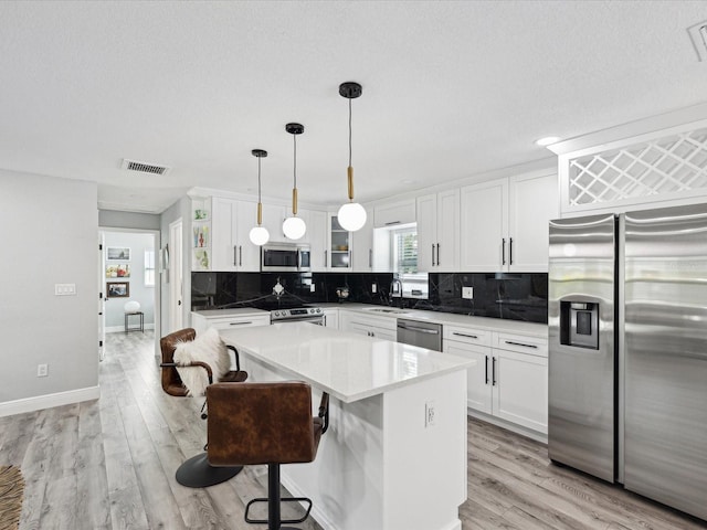 kitchen featuring appliances with stainless steel finishes, a center island, hanging light fixtures, and white cabinets