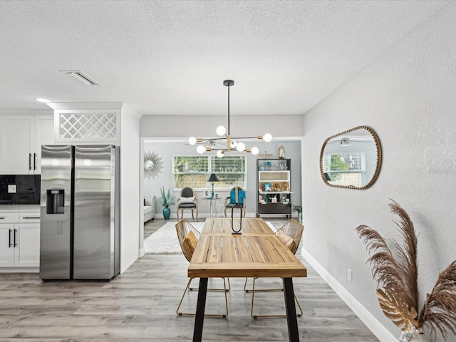 dining space with a notable chandelier, a textured ceiling, and light hardwood / wood-style flooring