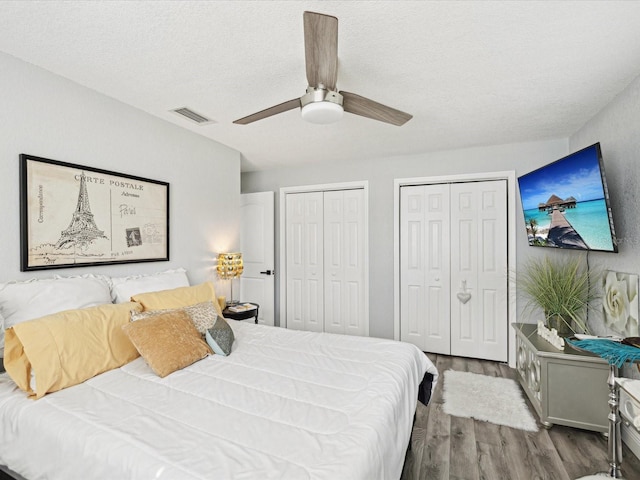 bedroom featuring multiple closets, ceiling fan, light hardwood / wood-style floors, and a textured ceiling