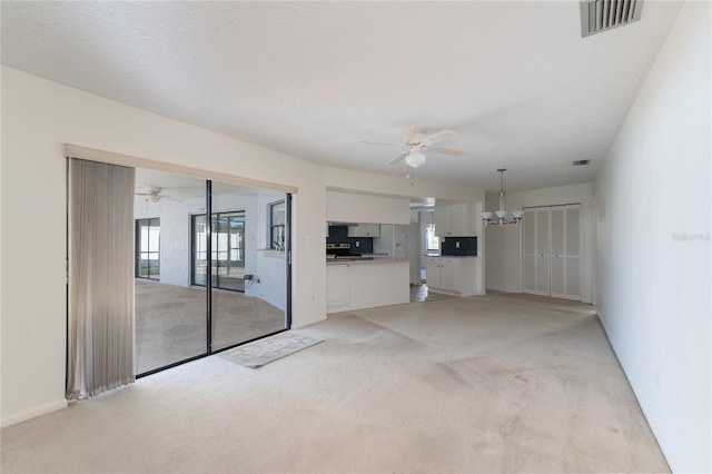 unfurnished living room featuring light carpet, ceiling fan with notable chandelier, and a textured ceiling