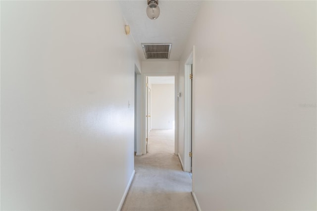 corridor with light colored carpet and a textured ceiling