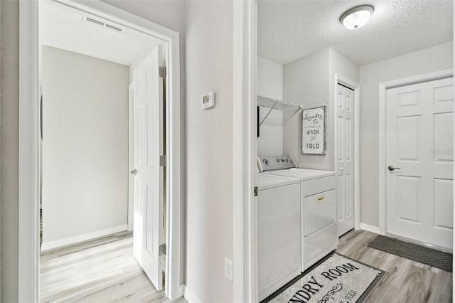 laundry room with light hardwood / wood-style floors, washer and dryer, and a textured ceiling