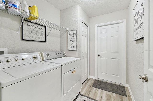 laundry area with a textured ceiling, washer and dryer, and light hardwood / wood-style flooring