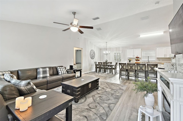 living room with sink, ceiling fan with notable chandelier, and light wood-type flooring