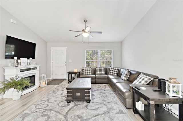 living room featuring ceiling fan, a high end fireplace, vaulted ceiling, and light hardwood / wood-style flooring