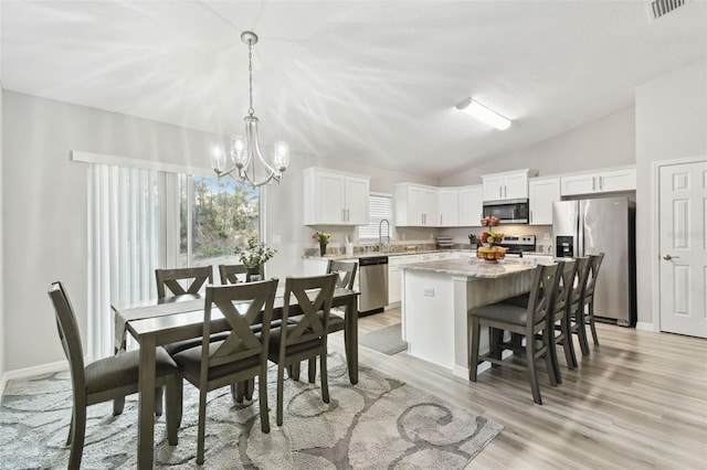 kitchen featuring a kitchen island, appliances with stainless steel finishes, pendant lighting, white cabinetry, and a chandelier