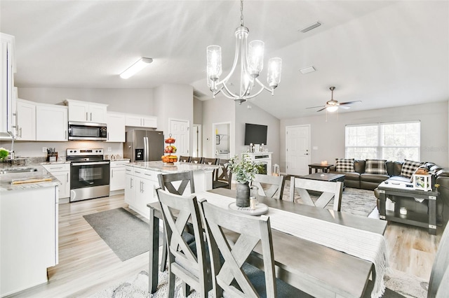 dining area with sink, ceiling fan with notable chandelier, vaulted ceiling, and light hardwood / wood-style floors