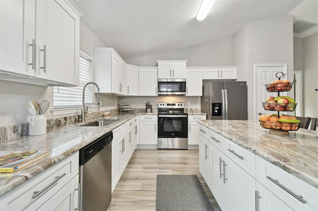 kitchen featuring sink, vaulted ceiling, white cabinets, and appliances with stainless steel finishes