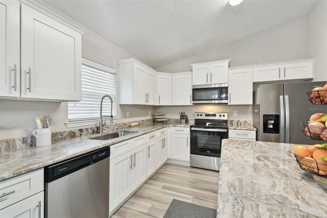 kitchen with lofted ceiling, stainless steel appliances, sink, and white cabinets