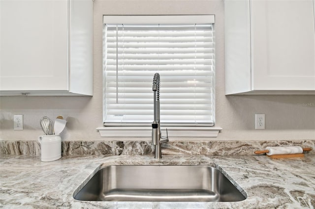 room details featuring light stone countertops, sink, and white cabinets