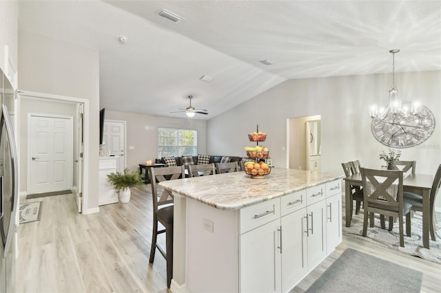 kitchen with a kitchen bar, white cabinetry, a kitchen island, pendant lighting, and light stone countertops