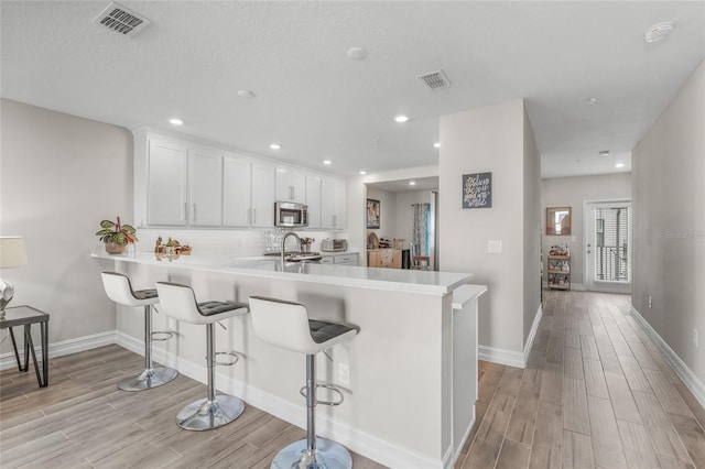 kitchen featuring light hardwood / wood-style floors, kitchen peninsula, white cabinets, and a breakfast bar