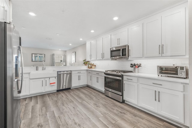 kitchen with appliances with stainless steel finishes, sink, white cabinets, light hardwood / wood-style floors, and kitchen peninsula