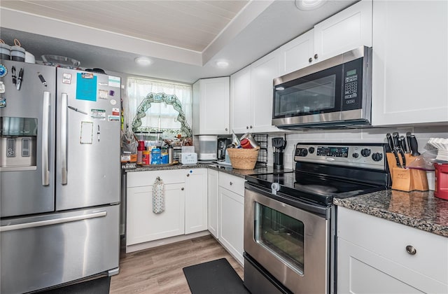 kitchen featuring stainless steel appliances, white cabinets, light wood-type flooring, and dark stone counters