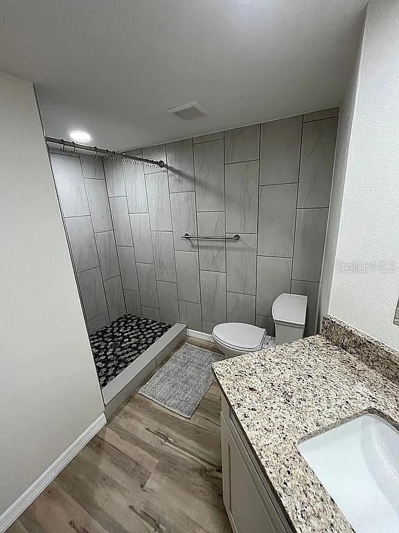 bathroom featuring wood-type flooring, toilet, vanity, and a tile shower