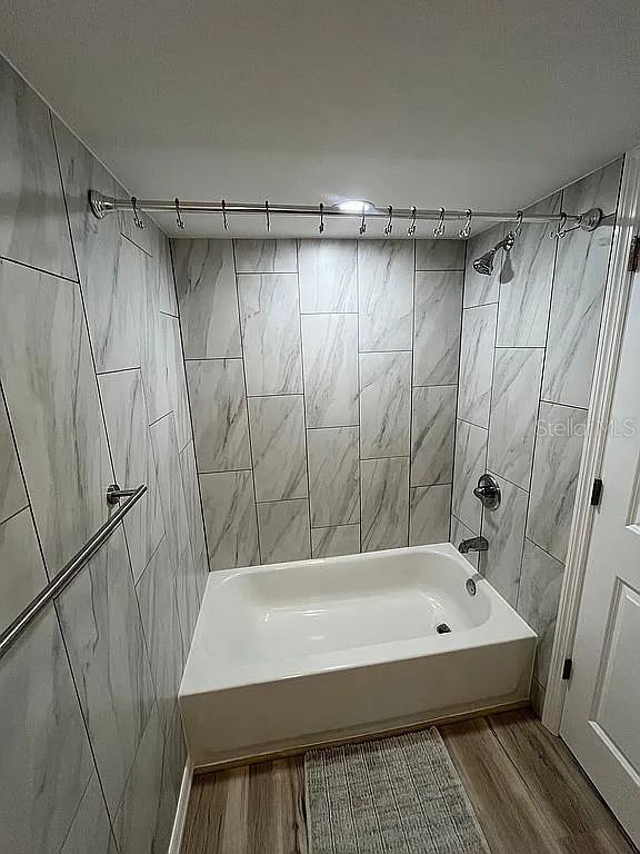 bathroom with tiled shower / bath, wood-type flooring, and tile walls