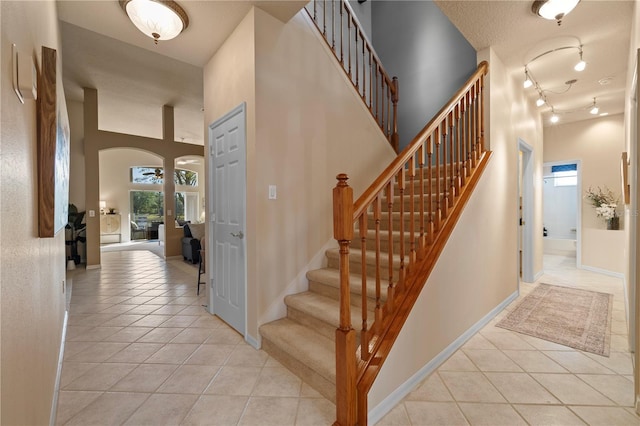 stairway with tile patterned floors, rail lighting, a textured ceiling, and a high ceiling