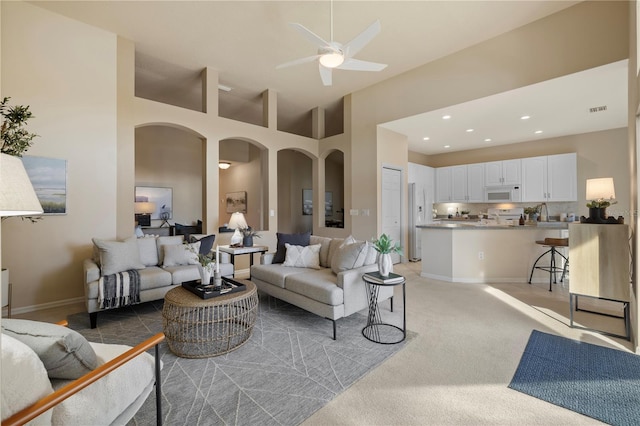 living room featuring a towering ceiling, light colored carpet, and ceiling fan