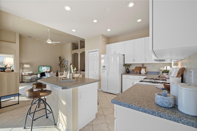 kitchen with light tile patterned flooring, white cabinetry, a breakfast bar area, white refrigerator with ice dispenser, and a center island