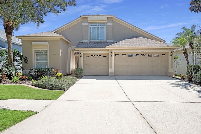 view of front facade with a shingled roof, concrete driveway, and stucco siding