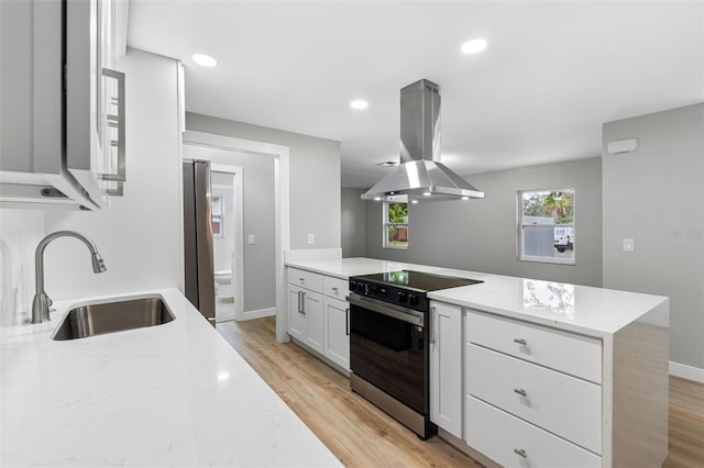 kitchen with island range hood, white cabinetry, sink, light stone counters, and electric stove