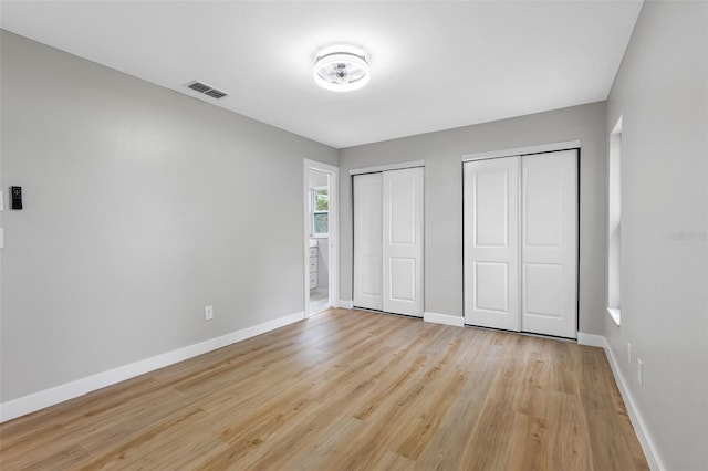 unfurnished bedroom with light hardwood / wood-style floors and two closets