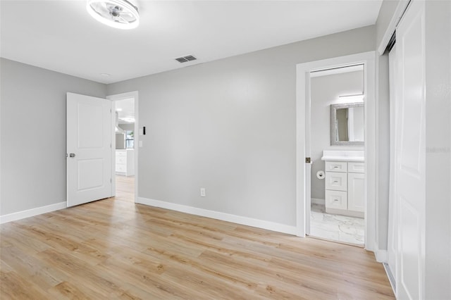 unfurnished bedroom with connected bathroom, a closet, and light wood-type flooring