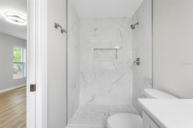 bathroom with a tile shower, hardwood / wood-style floors, vanity, and toilet