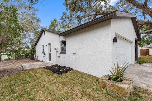 view of property exterior featuring a garage, cooling unit, and a lawn