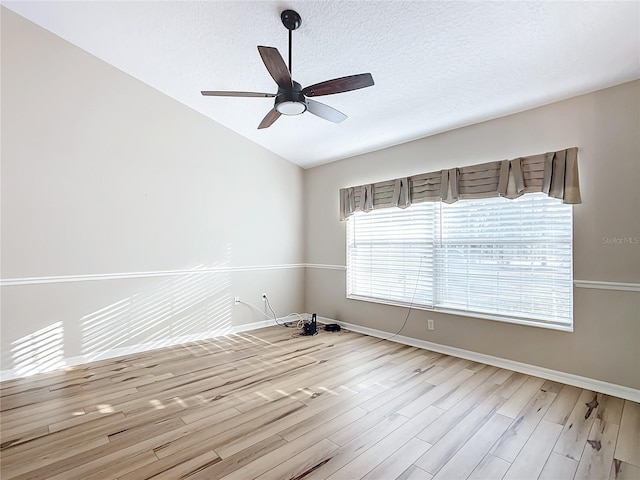 spare room featuring ceiling fan, lofted ceiling, a textured ceiling, and light wood-type flooring